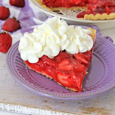 a slice of strawberry jello pie on a purple plate, topped with dollops of whipped cream