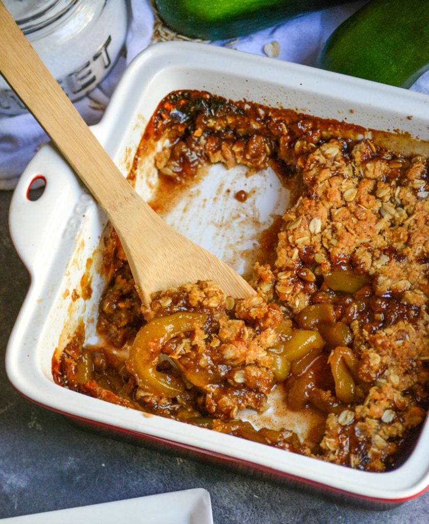 a wooden spoon shown scooping mock apple crisp out of a square casserole dish