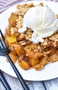 mock apple crisp on a small white dessert plate topped with a scoop of vanilla ice cream and a black fork on the side