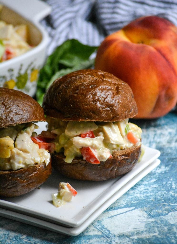 peach basil chicken salad shown on pumpernickel slider buns on a white appetizer plates