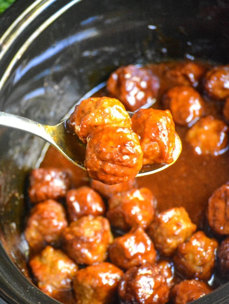 a silver serving spoon lifting several peach bourbon meatballs from a crockpot