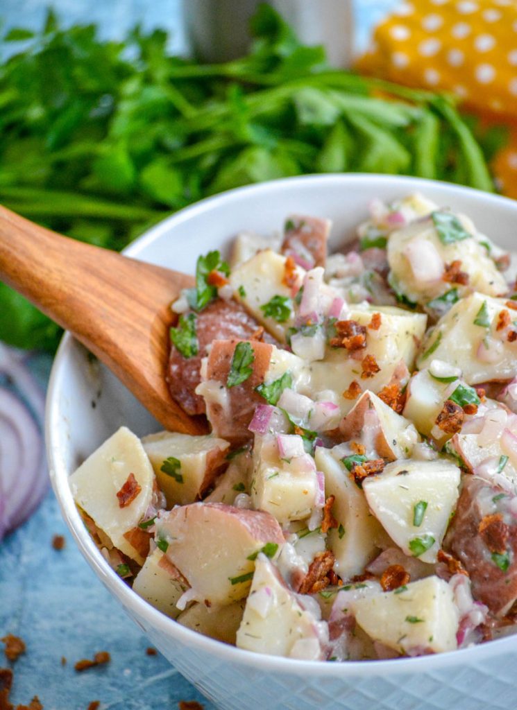 a wooden spoon shown scooping salt potato salad out of a white bowl