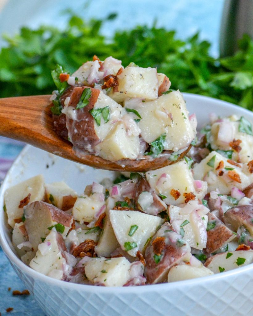 a wooden spoon shown scooping salt potato salad out of a white bowl