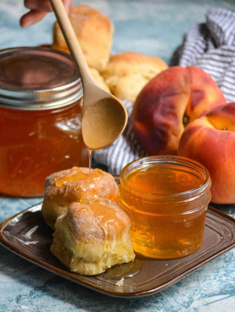 homemade peach syrup being spooned over buttermilk biscuits