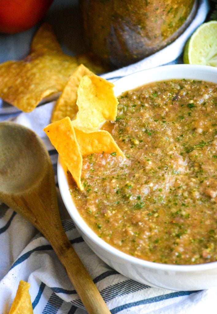 tortilla chips scooping smoked salsa out of a white serving bowl