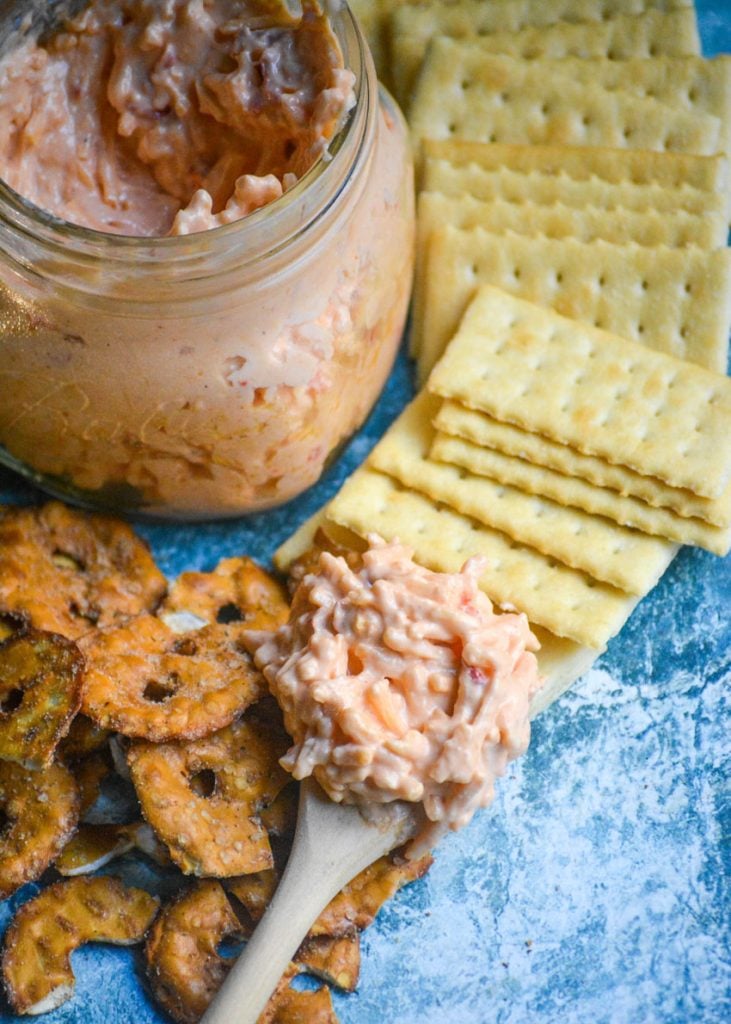 Southern style pimento cheese shown on a wooden spoon laid on top of pretzels and crackers