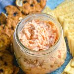 pimento cheese is shown in a glass mason jar surround by pretzels and crackers.