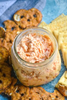 pimento cheese is shown in a glass mason jar surround by pretzels and crackers.