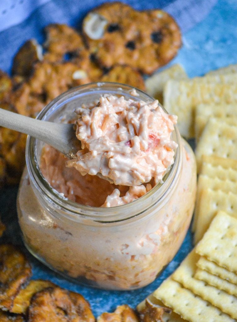 a wooden spoonful of pimento cheese being scooped out of a glass jar