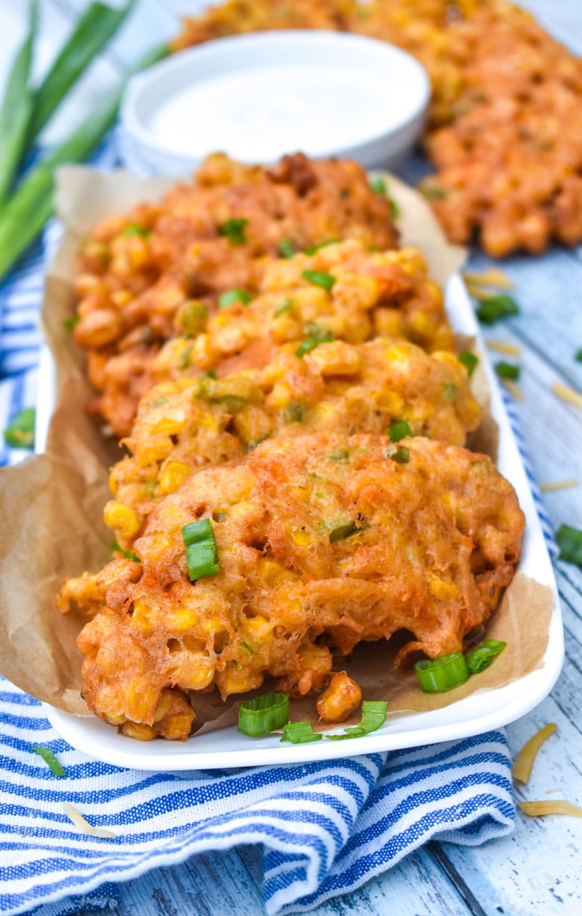 sweet corn and cheddar cheese fritters on a brown parchment paper lined white serving platter