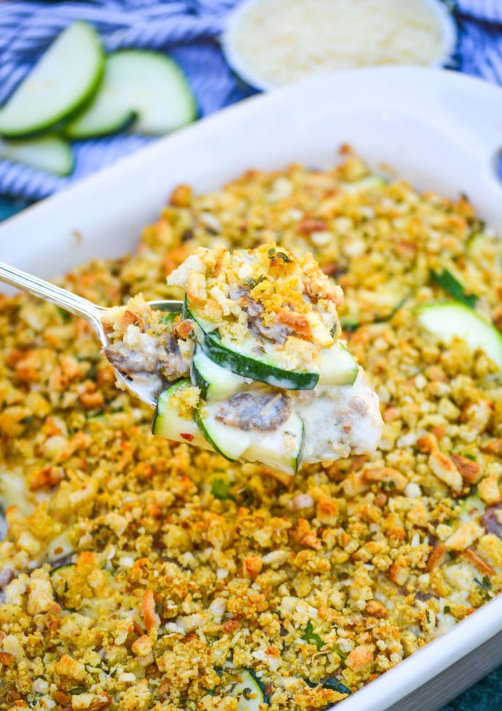 zucchini & sausage casserole being scooped out of an oval casserole dish on a silver spoon