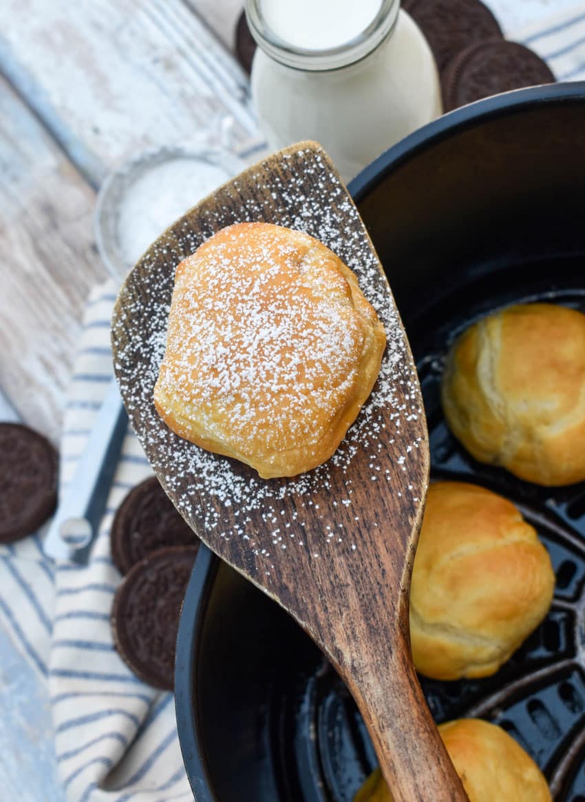 a wooden spatula holding up a powdered sugar dusted air fried oreo