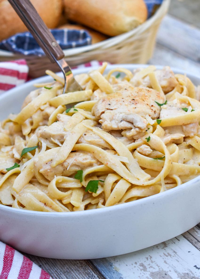 a fork scooping creamy cajun chicken alfredo in a gray bowl