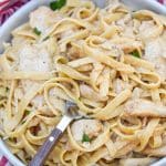 a fork scooping creamy cajun chicken alfredo in a gray bowl