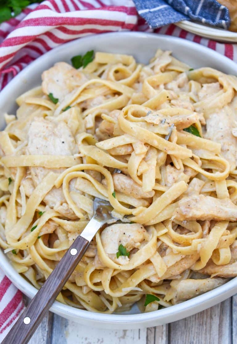 a fork scooping creamy cajun chicken alfredo in a gray bowl