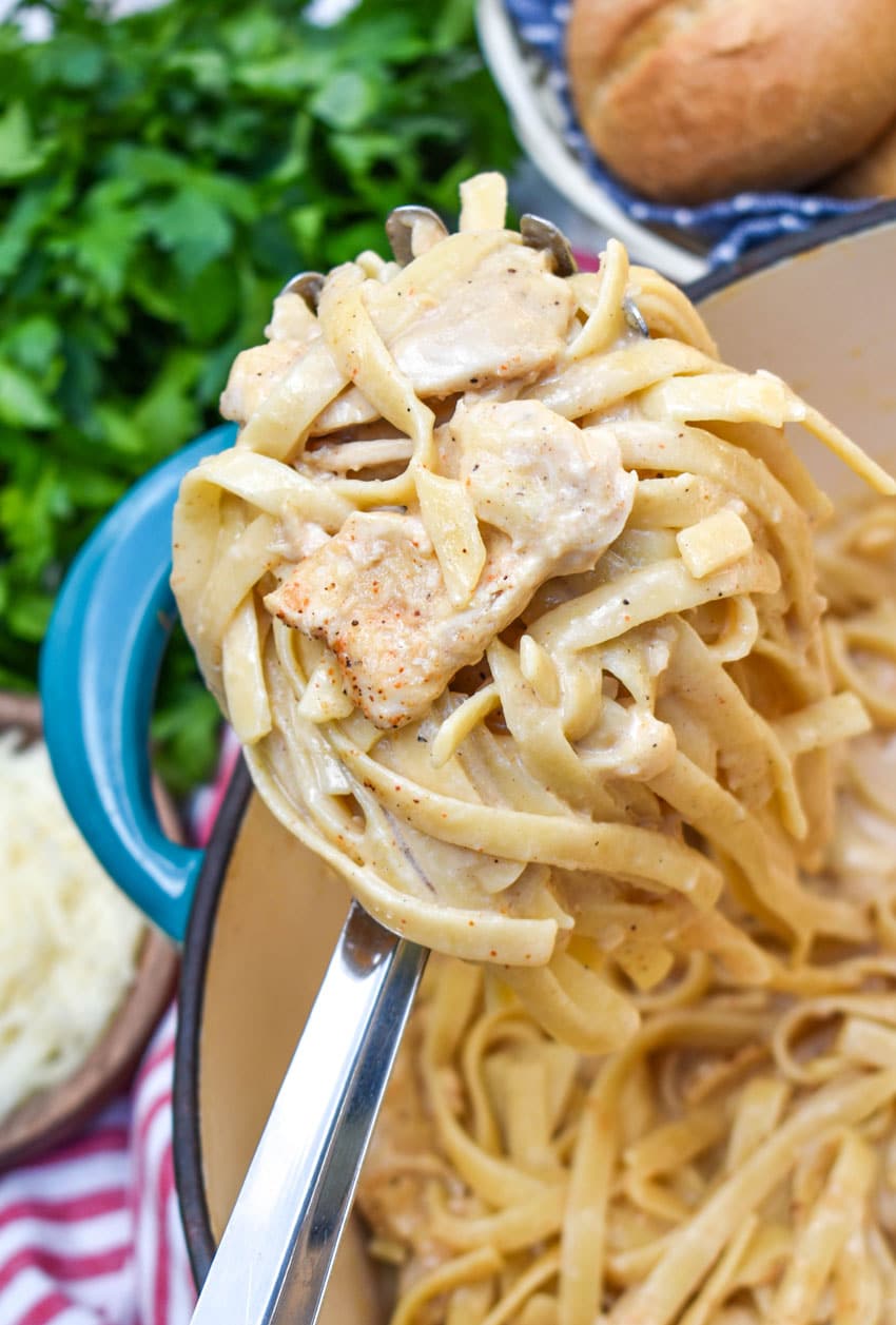 a silver spoon holding up a scoop of creamy cajun chicken alfredo pasta