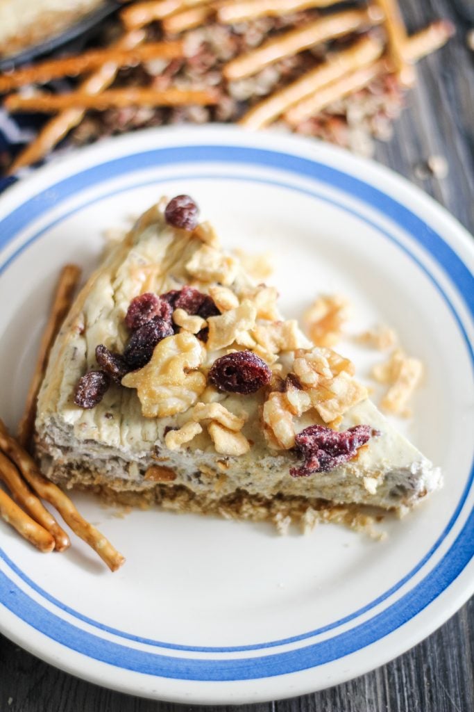 savory cheesecake served on a white plate and topped with chopped pecans and dried cranberries
