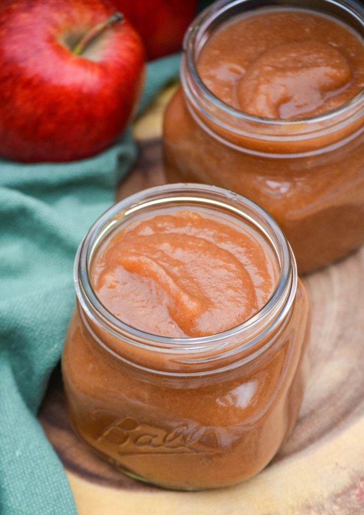 instant pot apple butter in glass mason jars sitting on a wooden cutting board in front of an instant pot