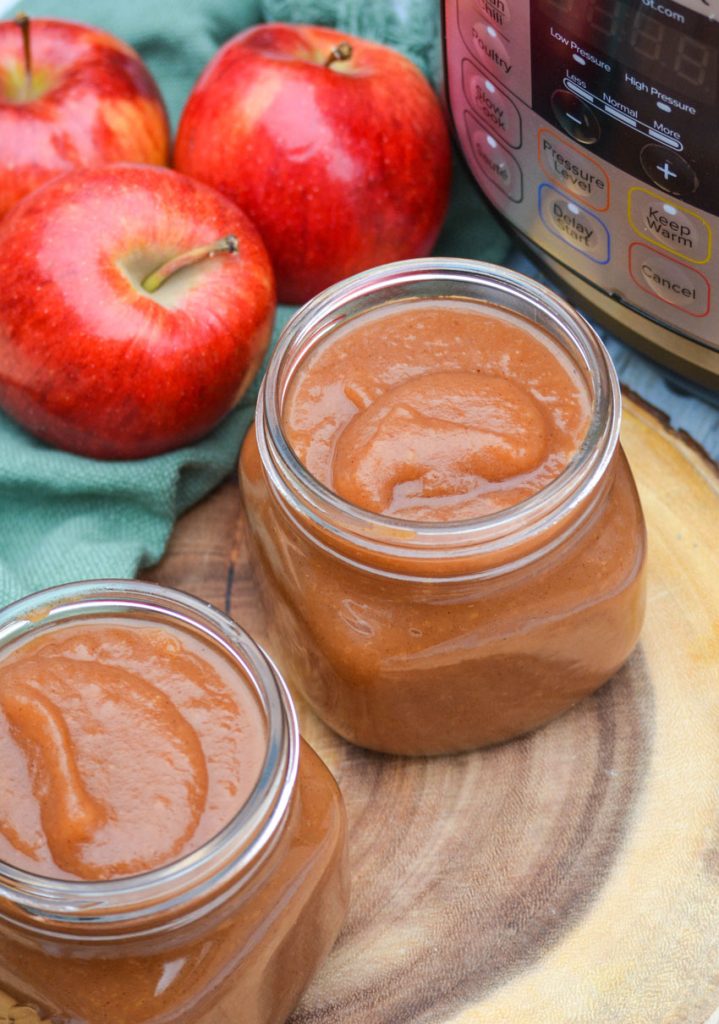 instant pot apple butter in glass mason jars sitting on a wooden cutting board in front of an instant pot