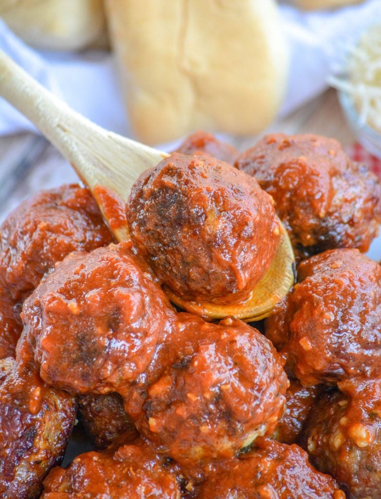 stacked, sauced cooked homemade meatballs shown with a wooden spoon