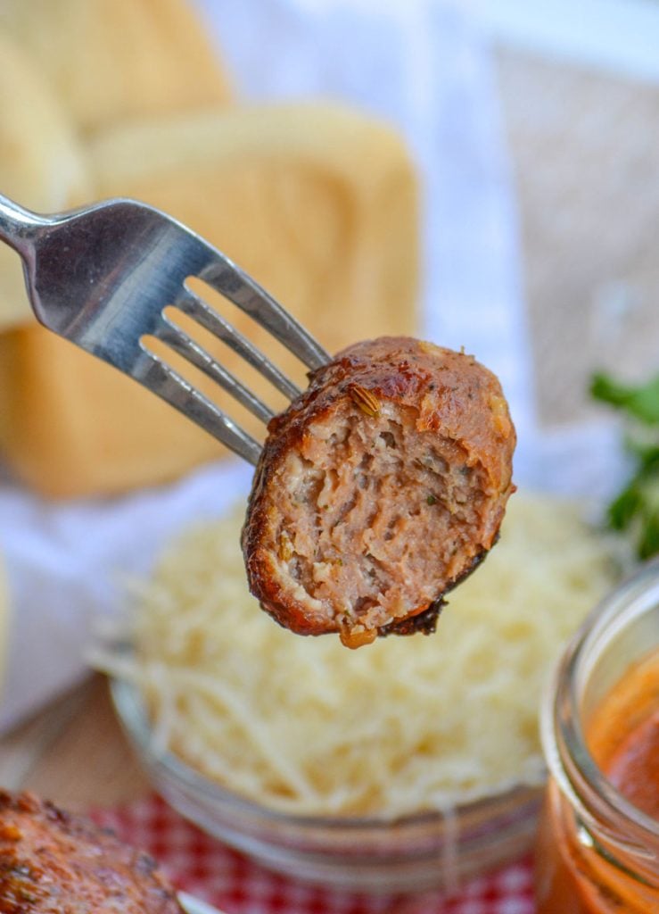 a bitten Italian meatball held aloft on a silver fork to reveal the inside