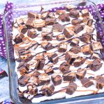 snickers poke cake made in a glass 9x13" baking dish with fun size snickers bars in the background