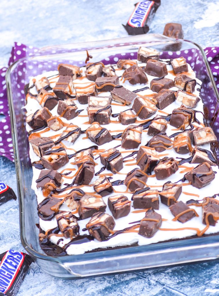 snickers poke cake made in a glass 9x13" baking dish with fun size snickers bars in the background
