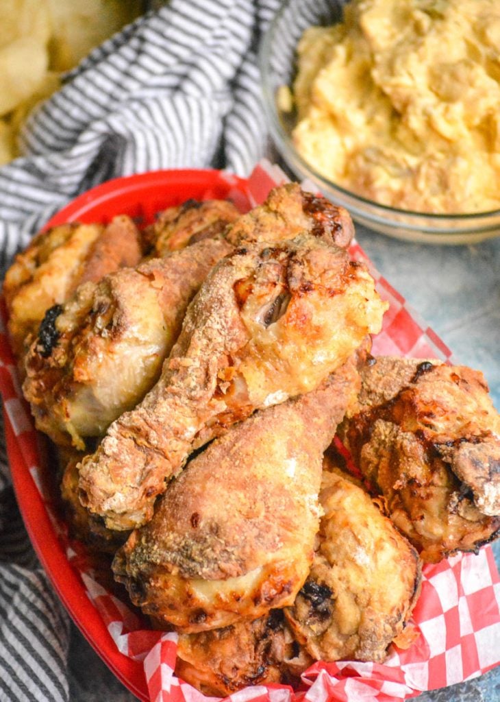 crispy air fryer fried chicken stacked in a paper lined red plastic basket with potato salad and hot sauce in the background