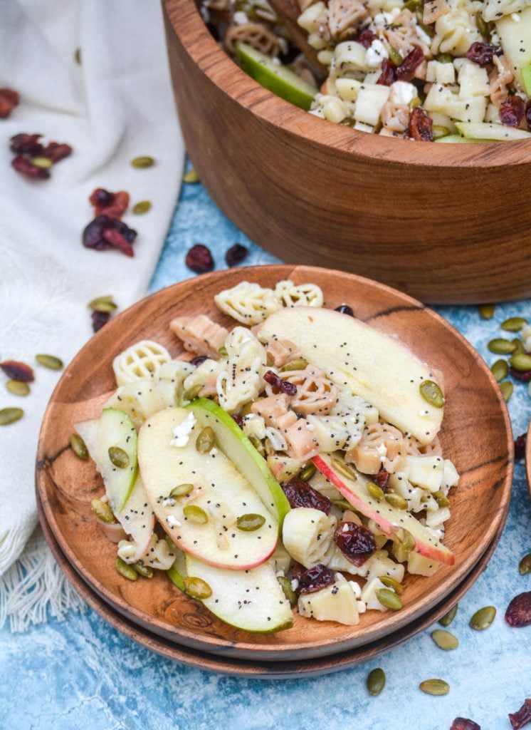 fall harvest pasta salad shown served on wooden plates and topped with dried cranberries, feta cheese, and pumpkin seeds