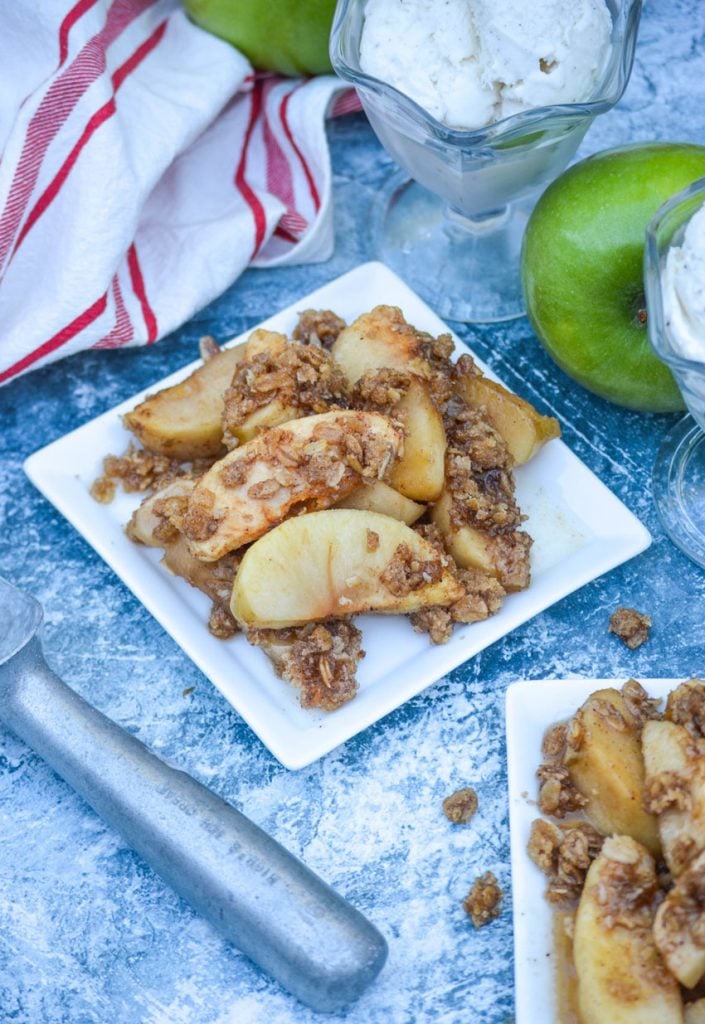 homemade apple crisp served on square white plates with bowls of ice cream and fresh apples in the background