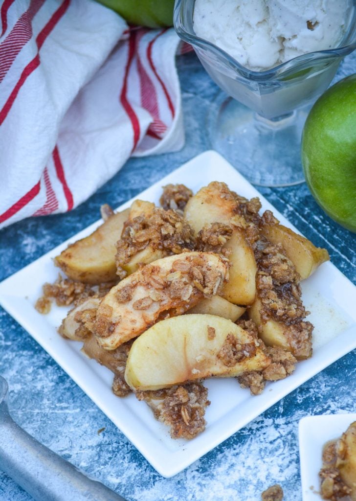 homemade apple crisp served on square white plates with bowls of ice cream and fresh apples in the background