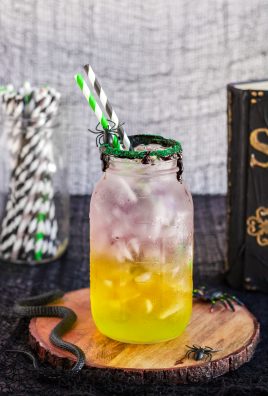 green, orange, and purple Halloween themed layered drink with ice in a glass mason jar rimmed with black icing and edible glitter
