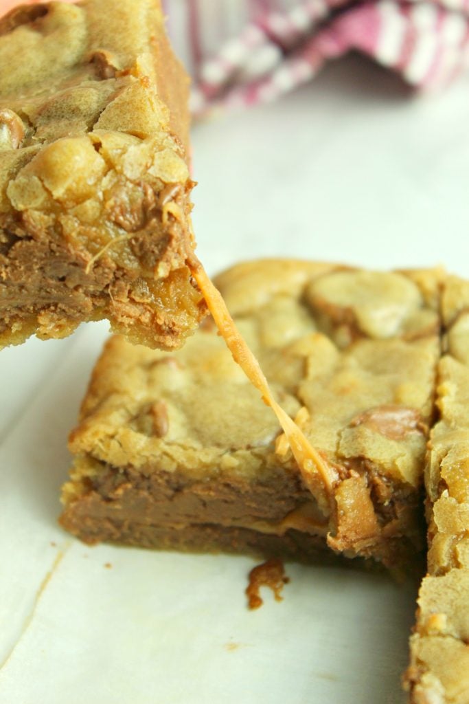 a rolo chocolate chip blondie being pulled away from the rest of the batch to show a thick strand of gooey, pulled caramel