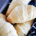 a pile of flaky, baked homemade crescent rolls in a cloth napkin lined metal loaf pan