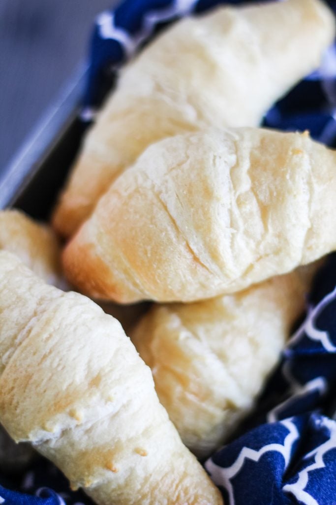 a pile of flaky, baked homemade crescent rolls in a cloth napkin lined metal loaf pan