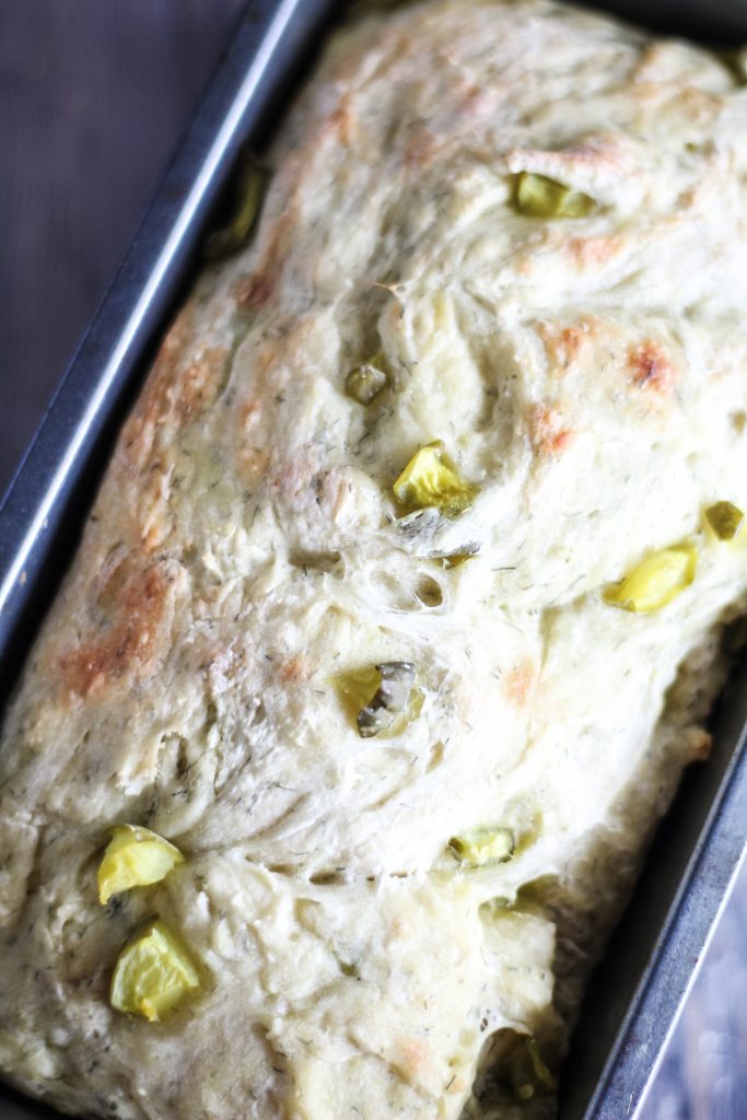 a loaf of dill pickle bread shown in a dark metal loaf pan