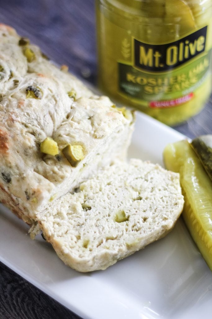 dill pickle bread shown sliced on a white serving platter with pickle spears on the side