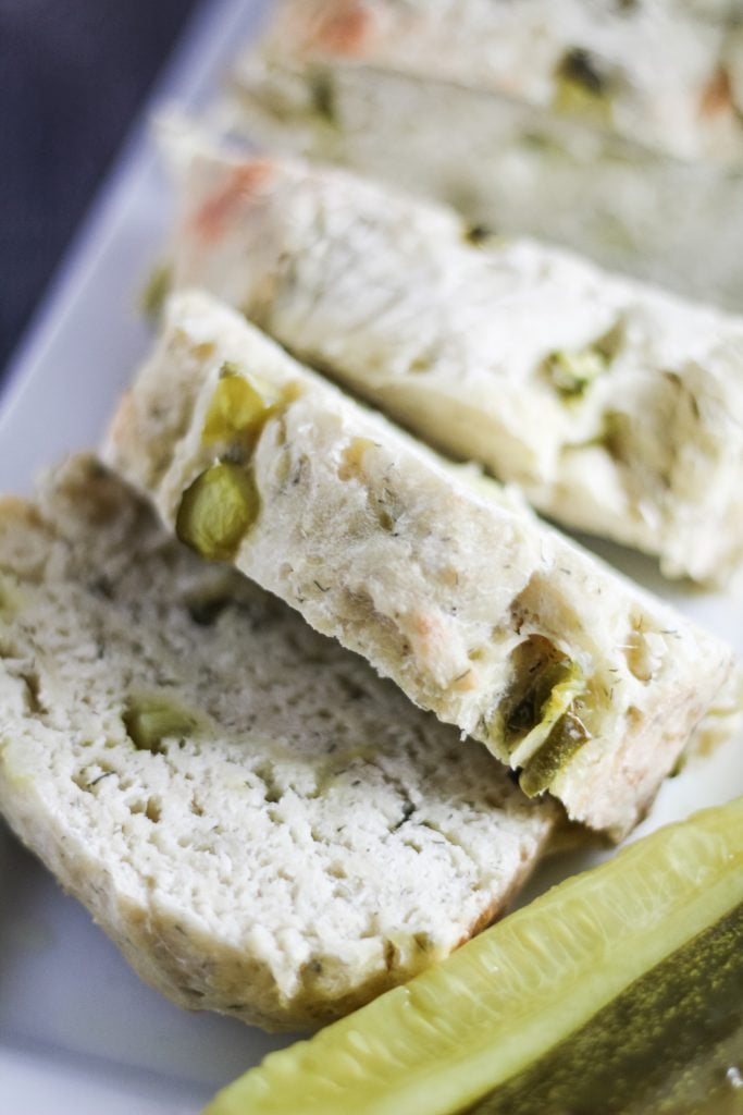 dill pickle bread shown sliced on a white serving platter with pickle spears on the side