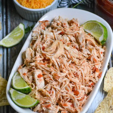 instant pot salsa chicken is shown shredded in a white corningware dish with fresh lime wedges