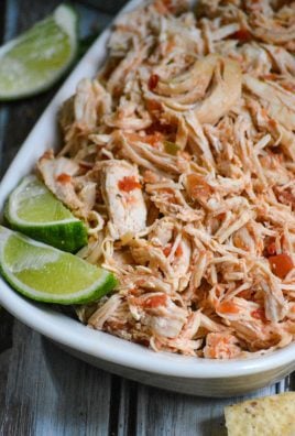 instant pot salsa chicken is shown shredded in a white corningware dish with fresh lime wedges