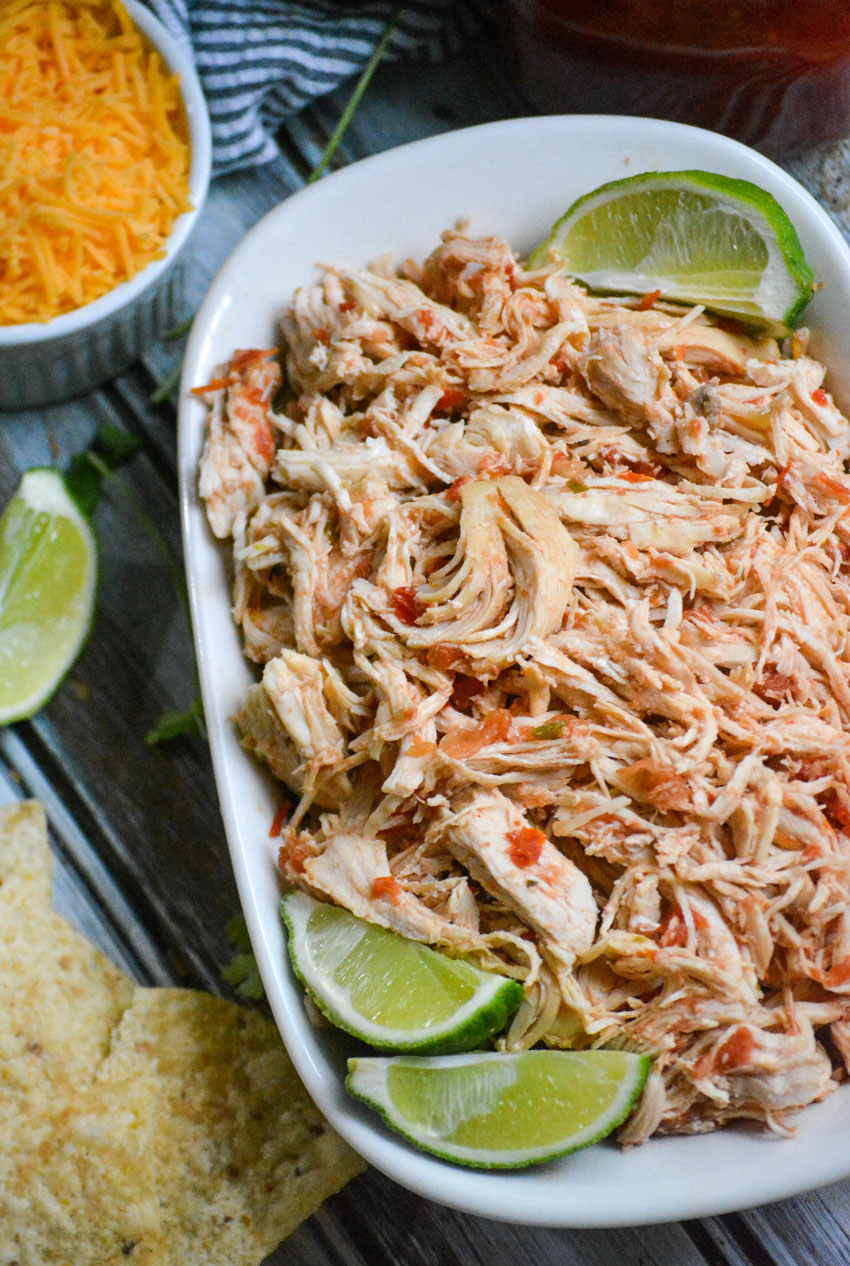 instant pot salsa chicken is shown shredded in a white corningware dish with fresh lime wedges