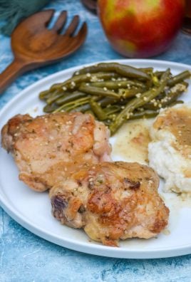 pan fried chicken thighs served on a white plate with apple cider gravy over mashed potatoes and green beans on the side