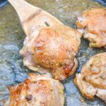 a wooden spoon holding up a pan fried chicken thigh that's been coated in apple cider gravy