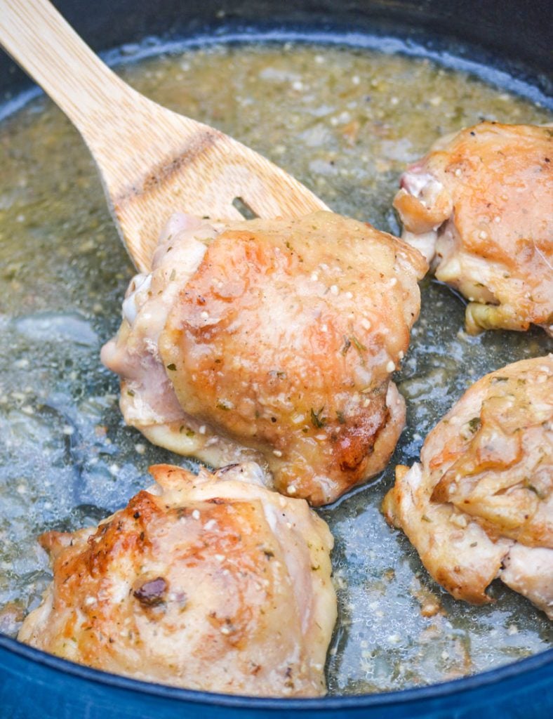 a wooden spoon holding up a pan fried chicken thigh that's been coated in apple cider gravy