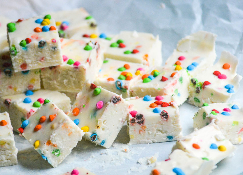 a pile of chunks of rainbow chip frosting, two ingredient fudge shown on a crinkled piece of white parchment paper