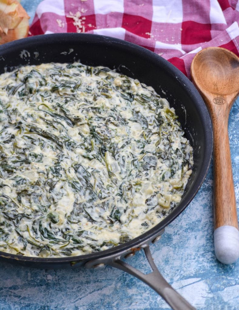 Morton's steakhouse style creamed spinach shown in a large black skillet with a wooden spoon off to the side for serving