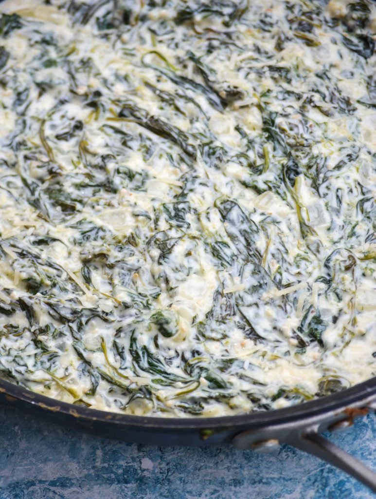a close up of cheesy creamed spinach in a large black skillet
