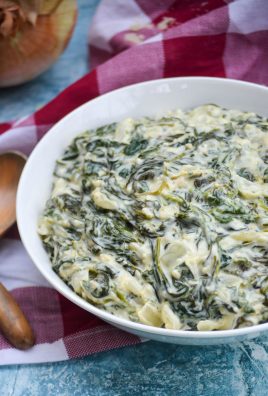 creamed spinach served in a shallow white bowl on a checkered cloth napkin with wooden spoons off to the side