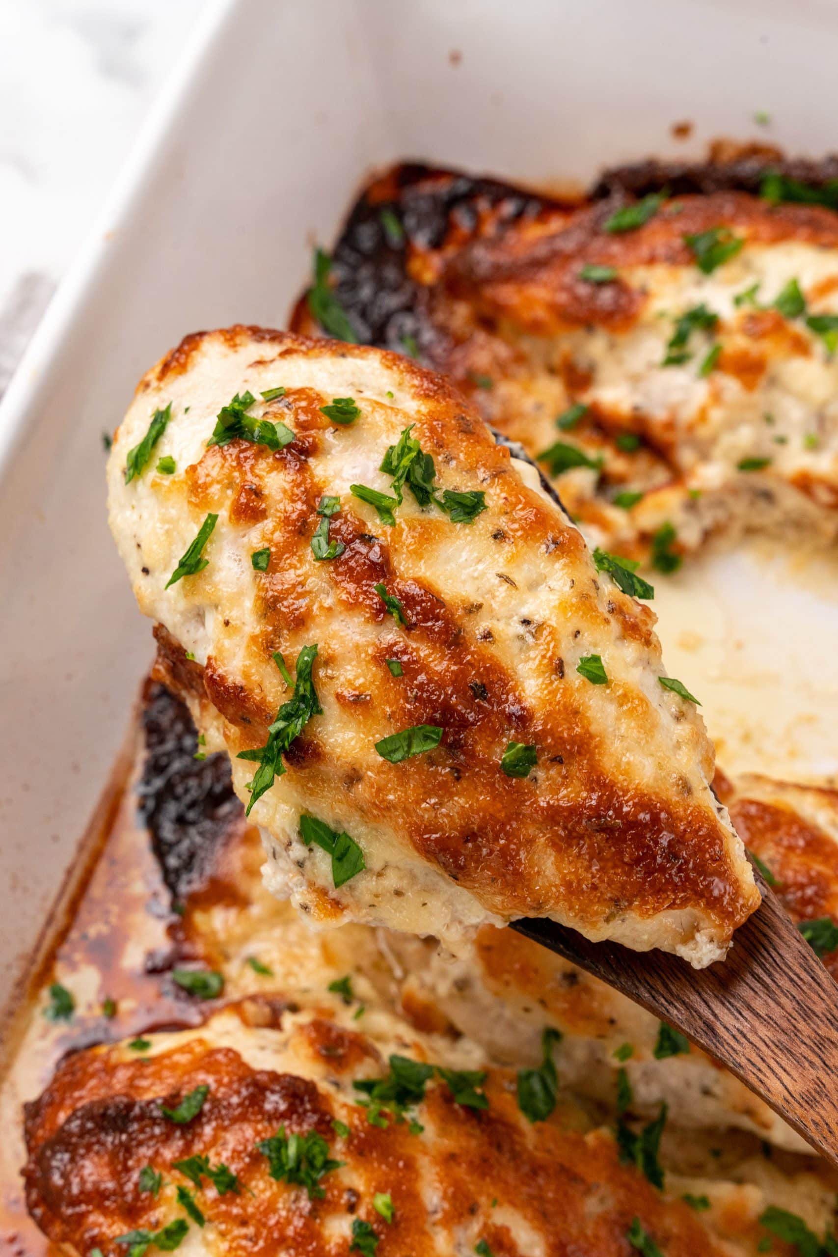 a wooden spoon holding up a piece of baked creamy parmesan chicken