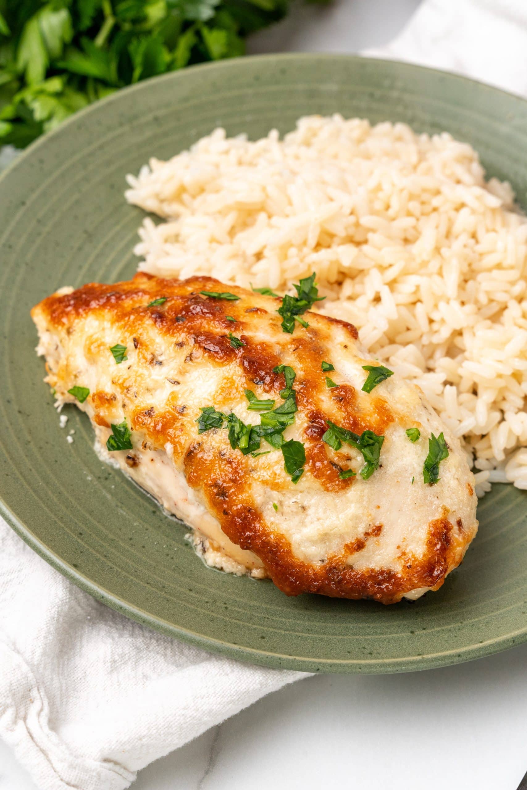 a slice of mayo parmesan chicken on a green plate with cooked rice on the side